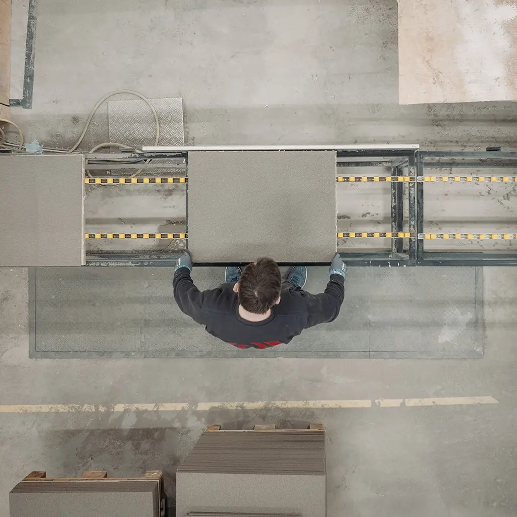 Employee handling an acoustic panel on a conveyor belt in production at Hz Acoustic, seen from above
